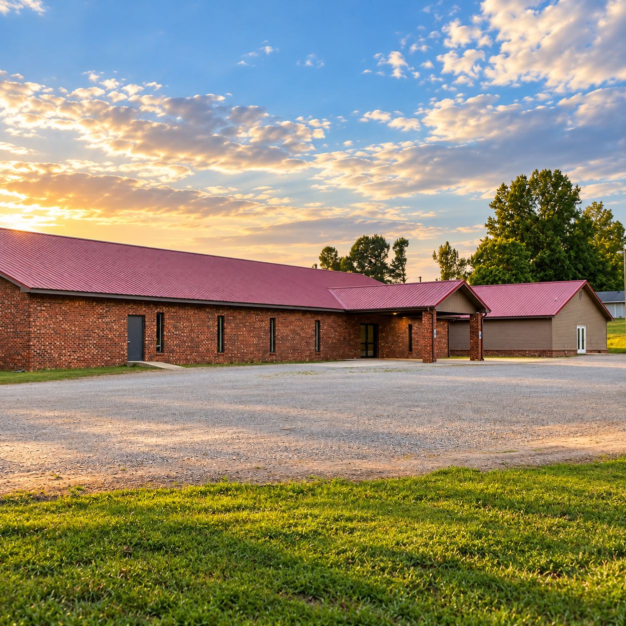 The Well Assembly of God: a long brick building with a red metal roof and a covered front entrance, at sunset.